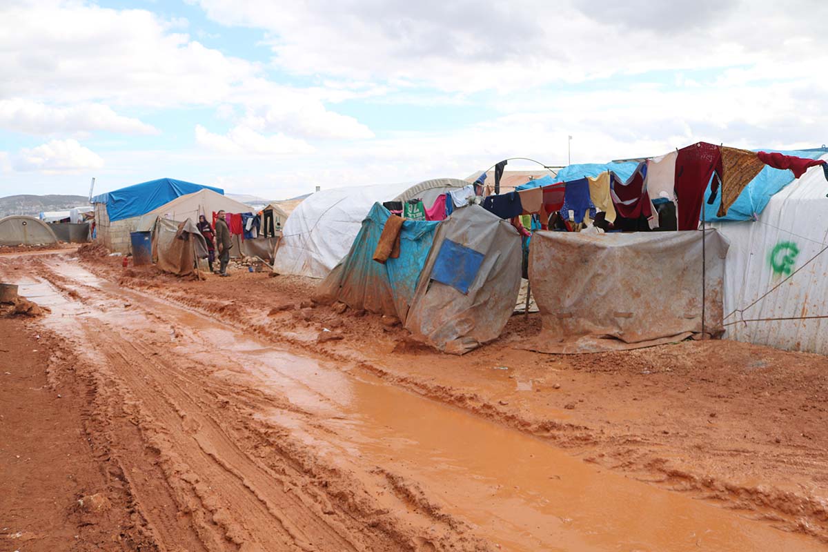 A muddy road lined with make-shift tent shelters