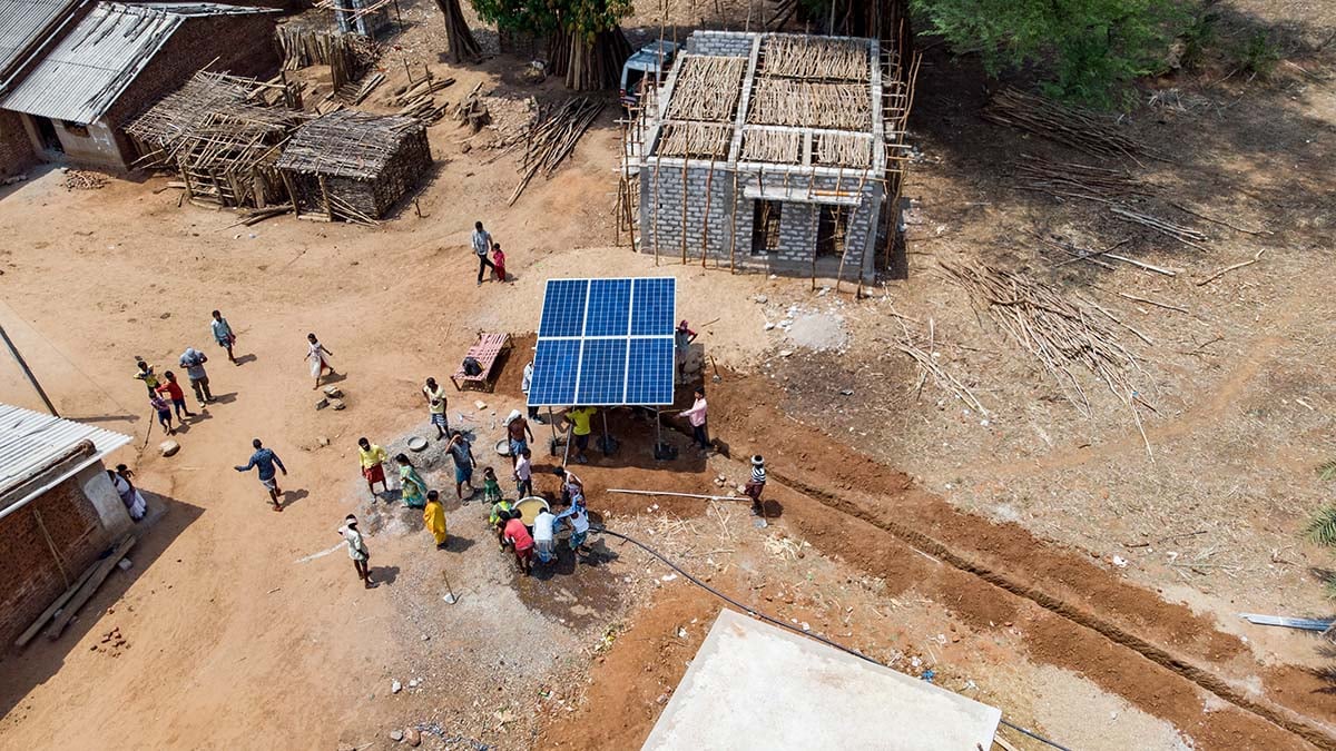 An aerial view of villagers gathered around elevated solar panels