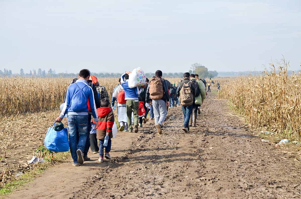 A procession of refugees walking down a dirt path